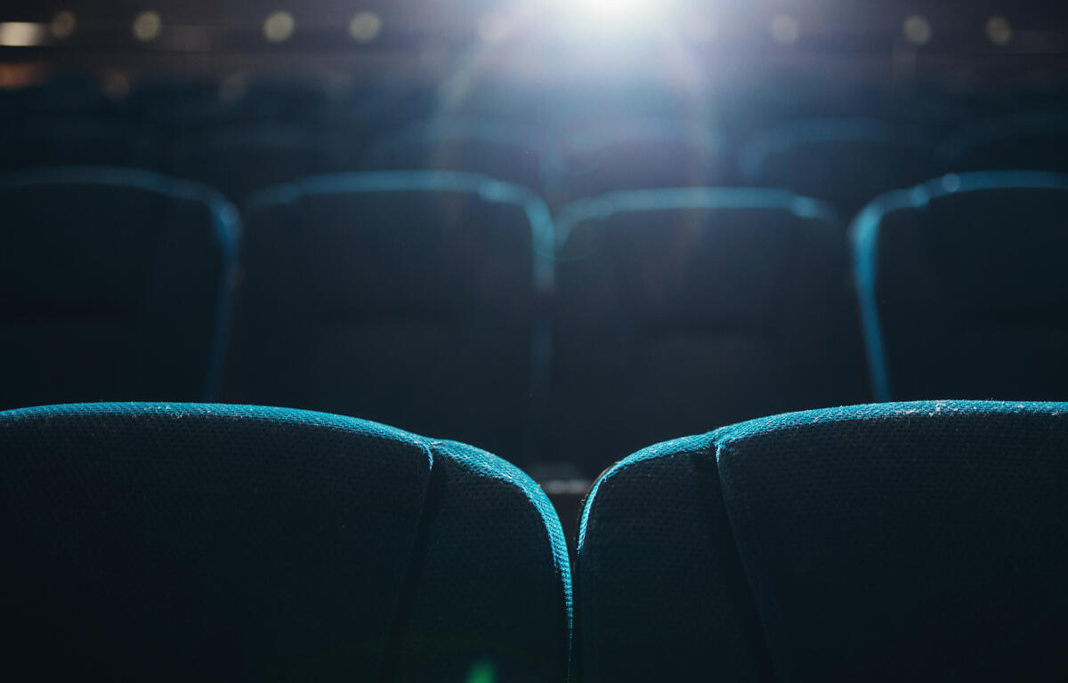 Empty rows of seats in cinema or theater with projector lighting from behind.