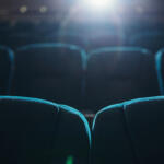 Empty rows of seats in cinema or theater with projector lighting from behind.