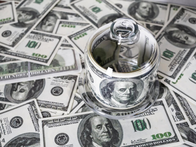 Money in a glass container on the background of one hundred dollar bills. Counterfeit money. Conceptual photo on the business theme. Selective focus.