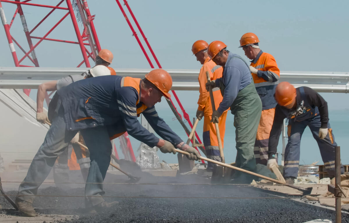 Several men pour and smooth pavement on a road.