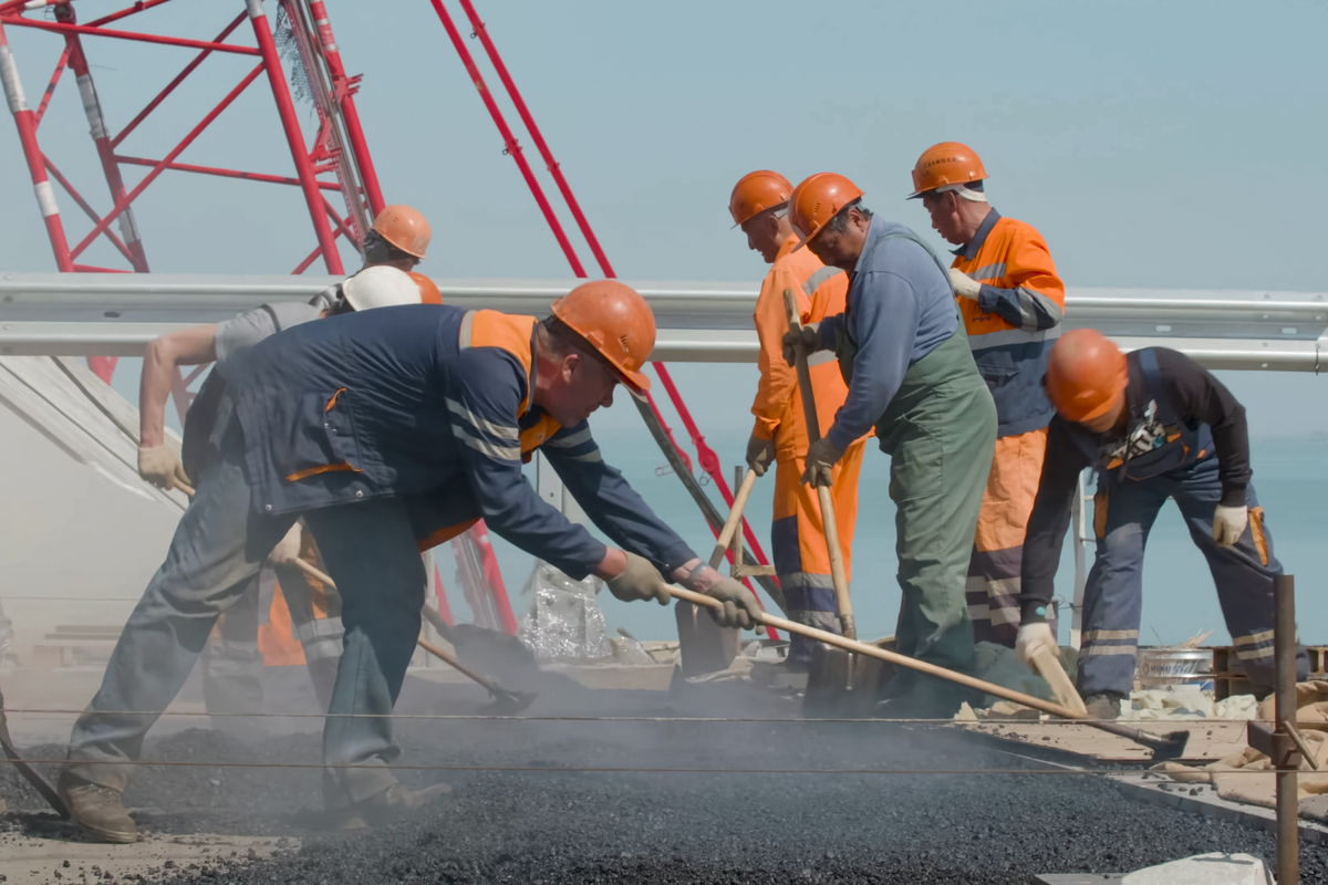 Several men pour and smooth pavement on a road.