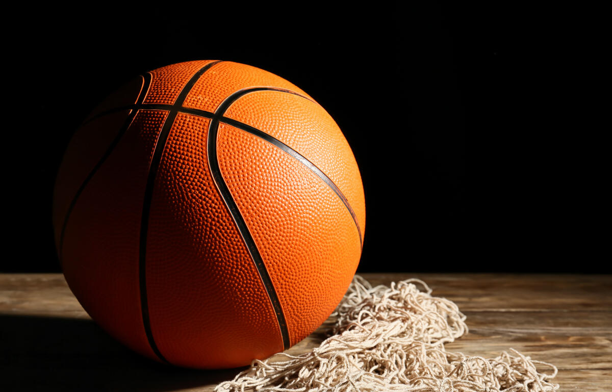 A basketball sitting on a net on a court floor.