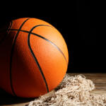 A basketball sitting on a net on a court floor.
