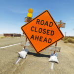 Road sign on rural highway warning that road is closed ahead.