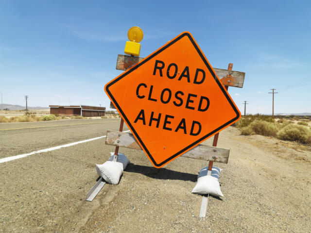 Road sign on rural highway warning that road is closed ahead.