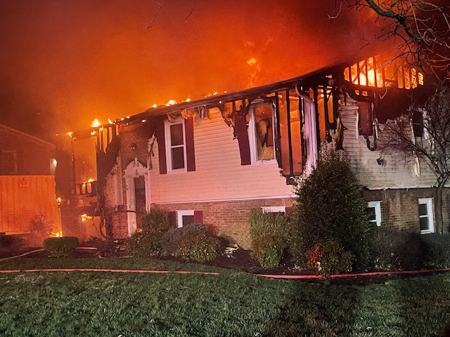 The front of a house on fire with siding melting off and flames coming from the roof.