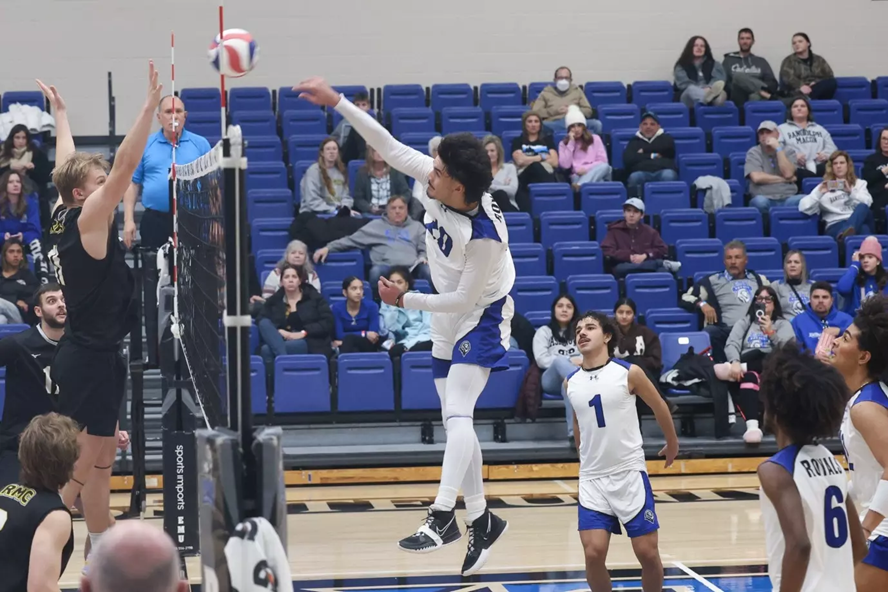 An Eastern Mennonite University volleyball player jumps in the air to spike the ball over the net.