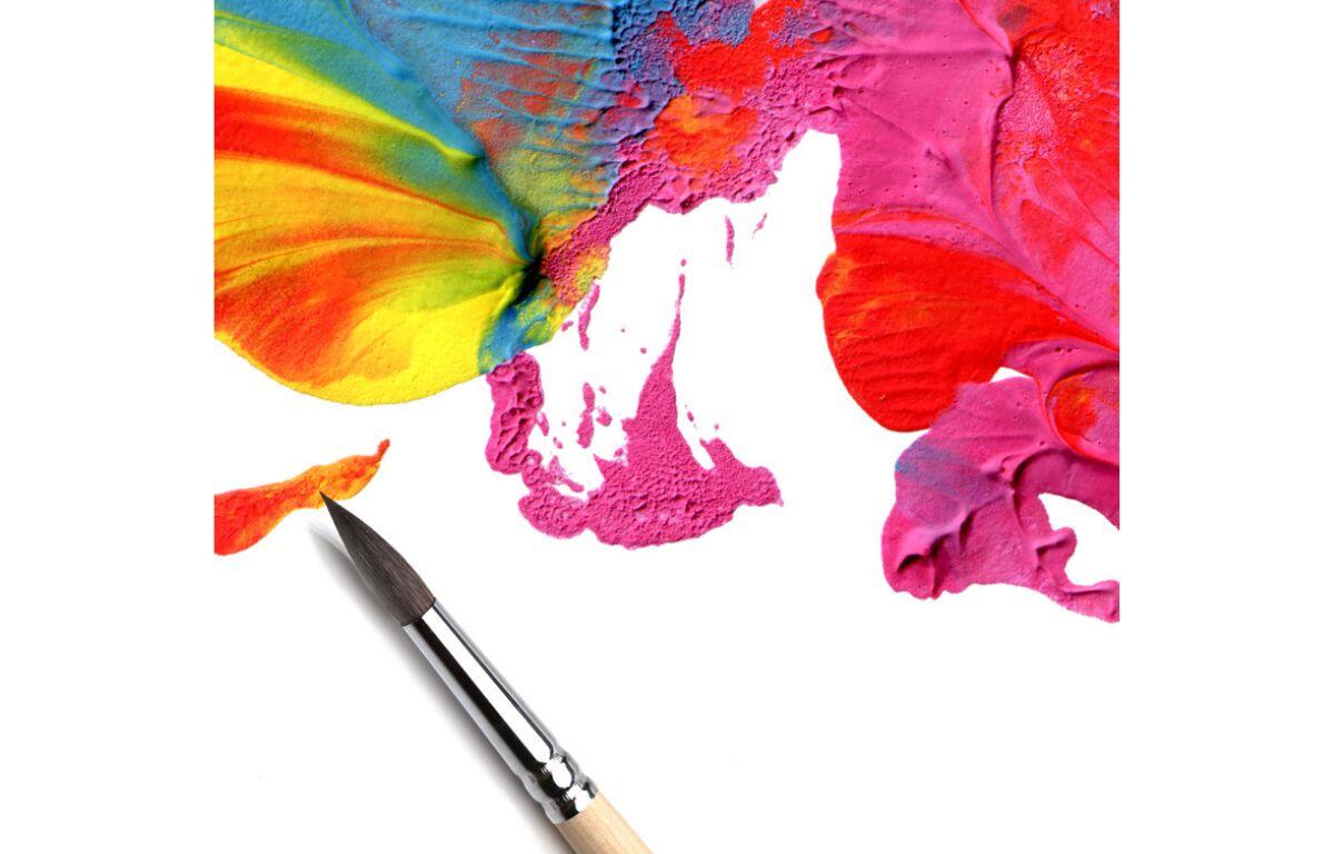 A picture of a paint brush laying on a canvas with rainbow paint smeared around it.