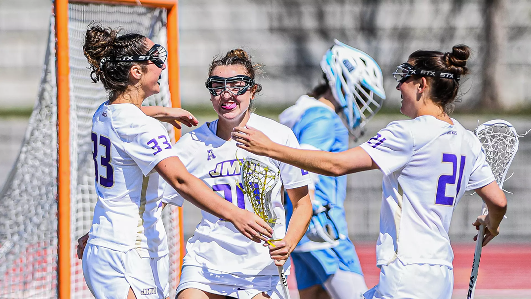 Three James Madison University lacrosse players huddle together