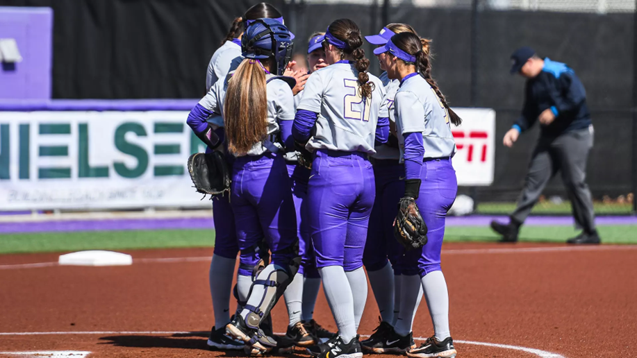 James Madison University softball players huddle together on the field.