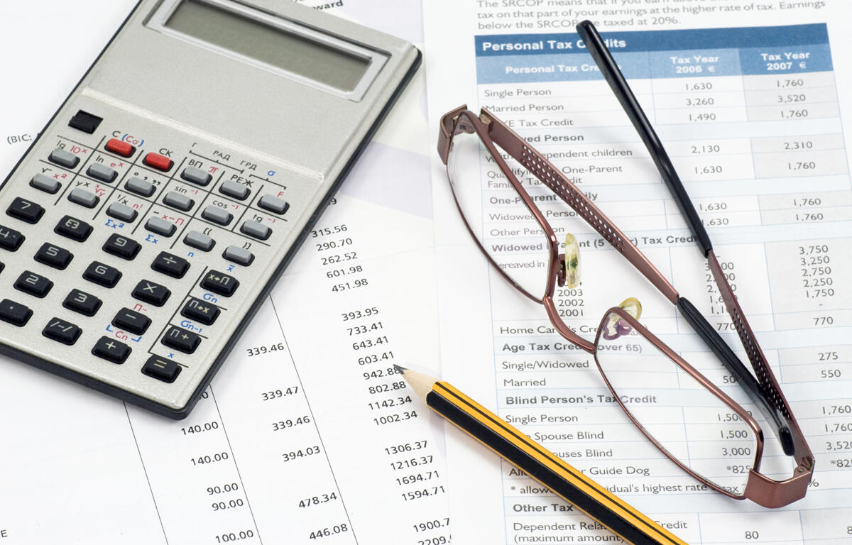 A calculator, glasses, and pencil lay on top of several scattered papers.