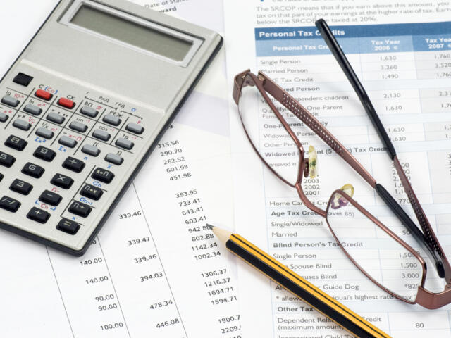 A calculator, glasses, and pencil lay on top of several scattered papers.
