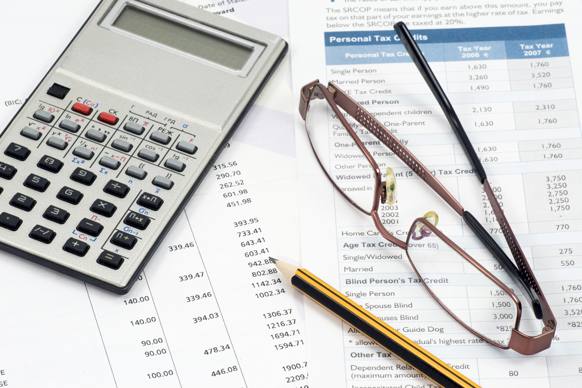 A calculator, glasses, and pencil lay on top of several scattered papers.