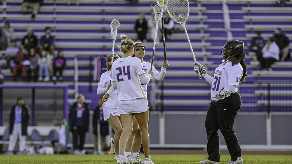 JMU Lacross teammates raising lacrosse sticks