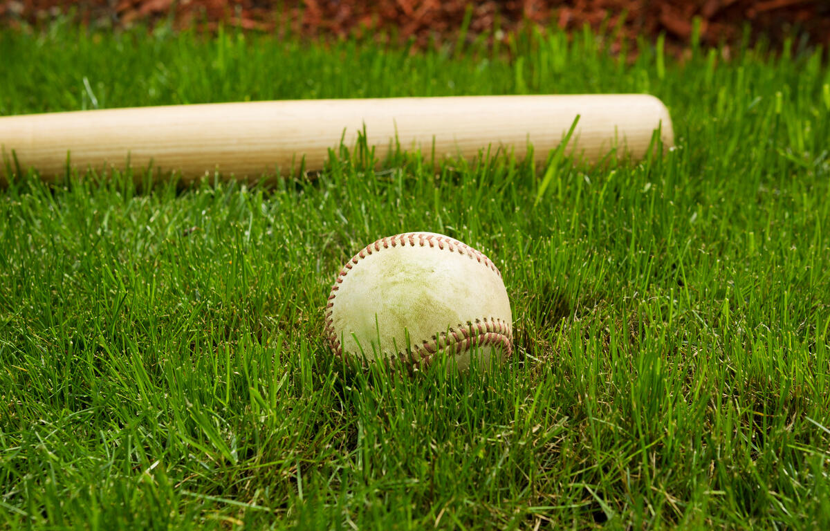 Closeup horizontal photo of old baseball in front of wooden bat on natural grass field