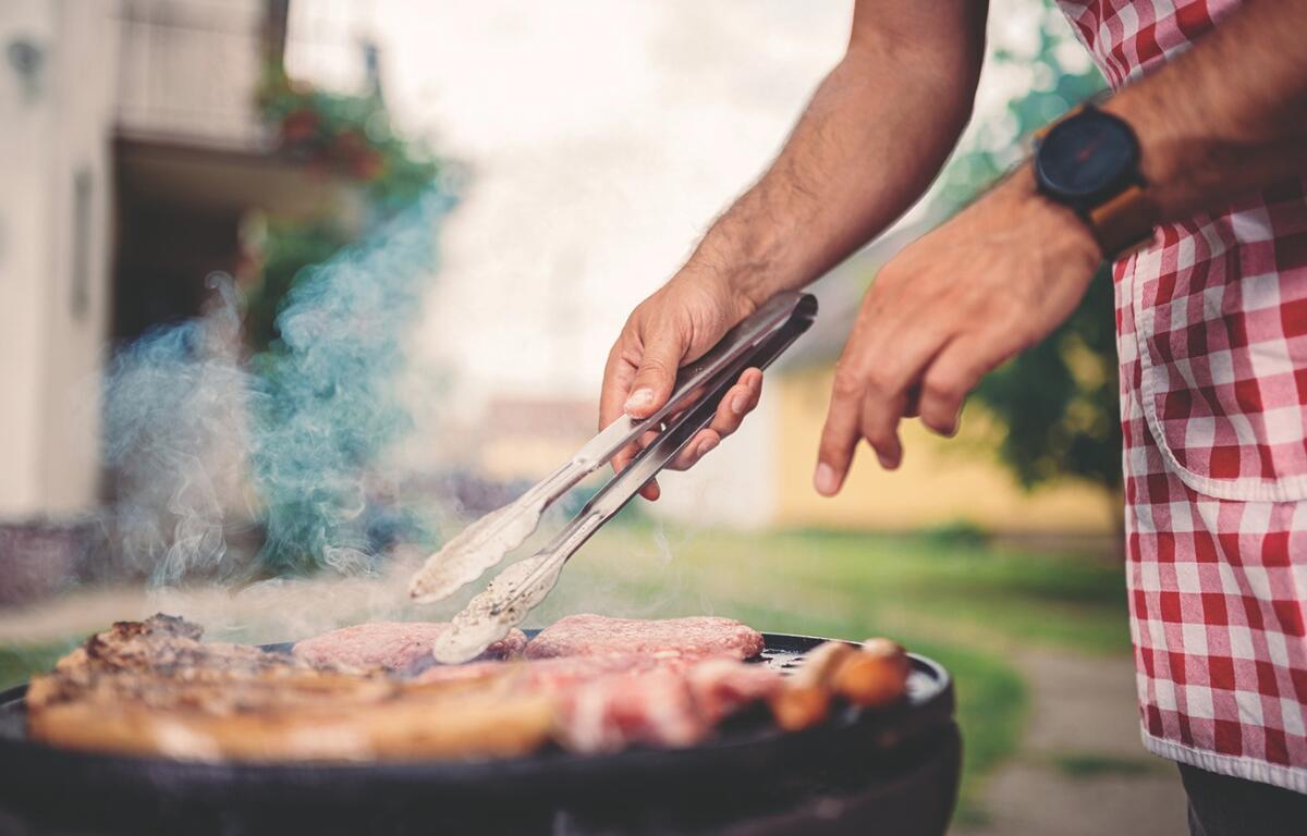 A person with tongs over a grill turning meat.