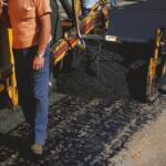 A construction worker lays pavement on a road.