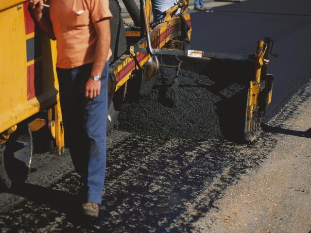 A construction worker lays pavement on a road.