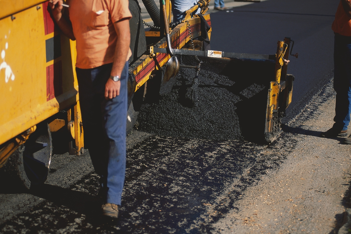 A construction worker lays pavement on a road.