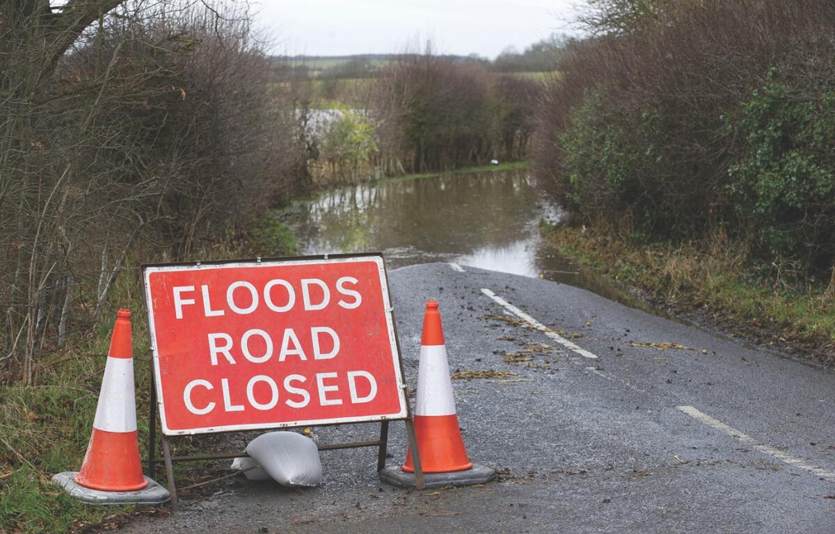 A road closed sign in front of a flooded road.