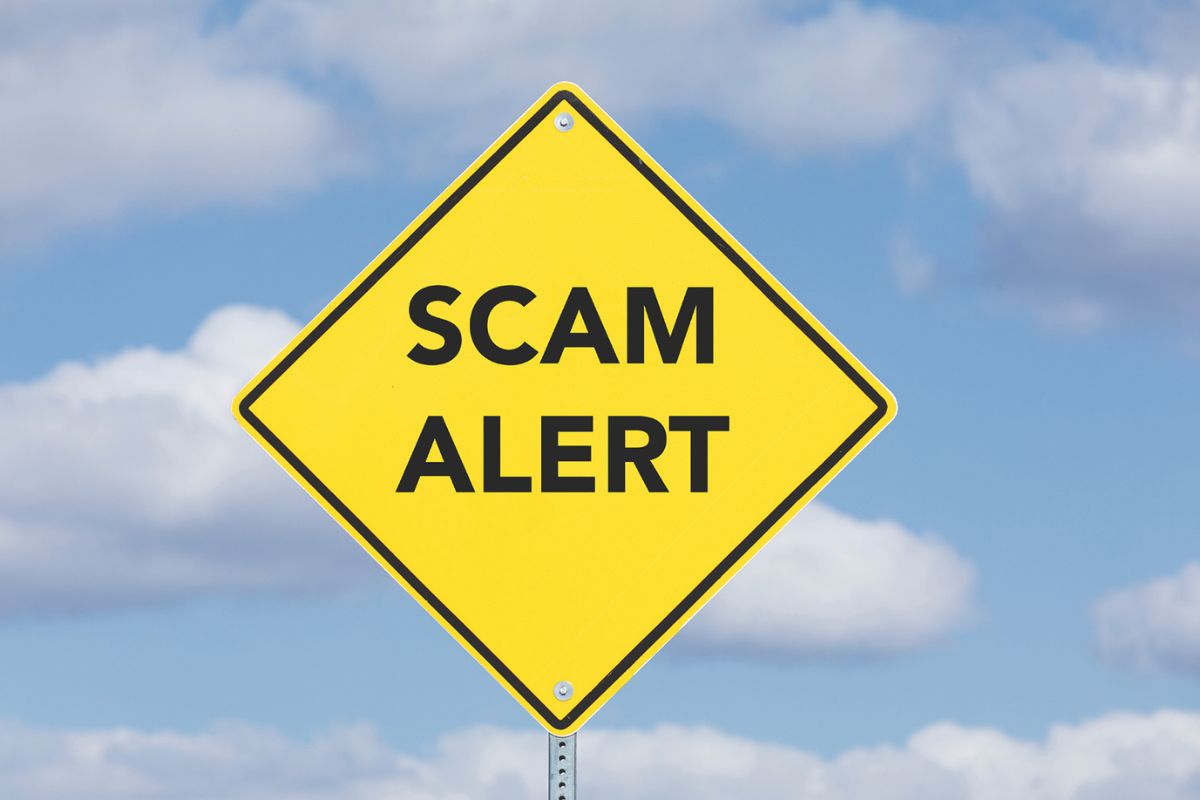 Scam Alert on yellow sign with clouds in the background