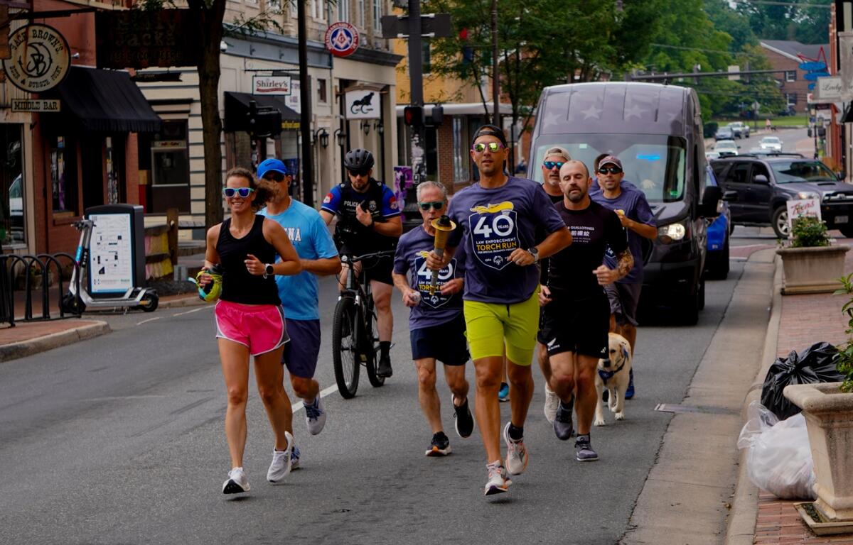 Officers and community members running down the street with police cars following them as they carry the torch.
