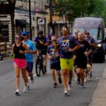 Officers and community members running down the street with police cars following them as they carry the torch.