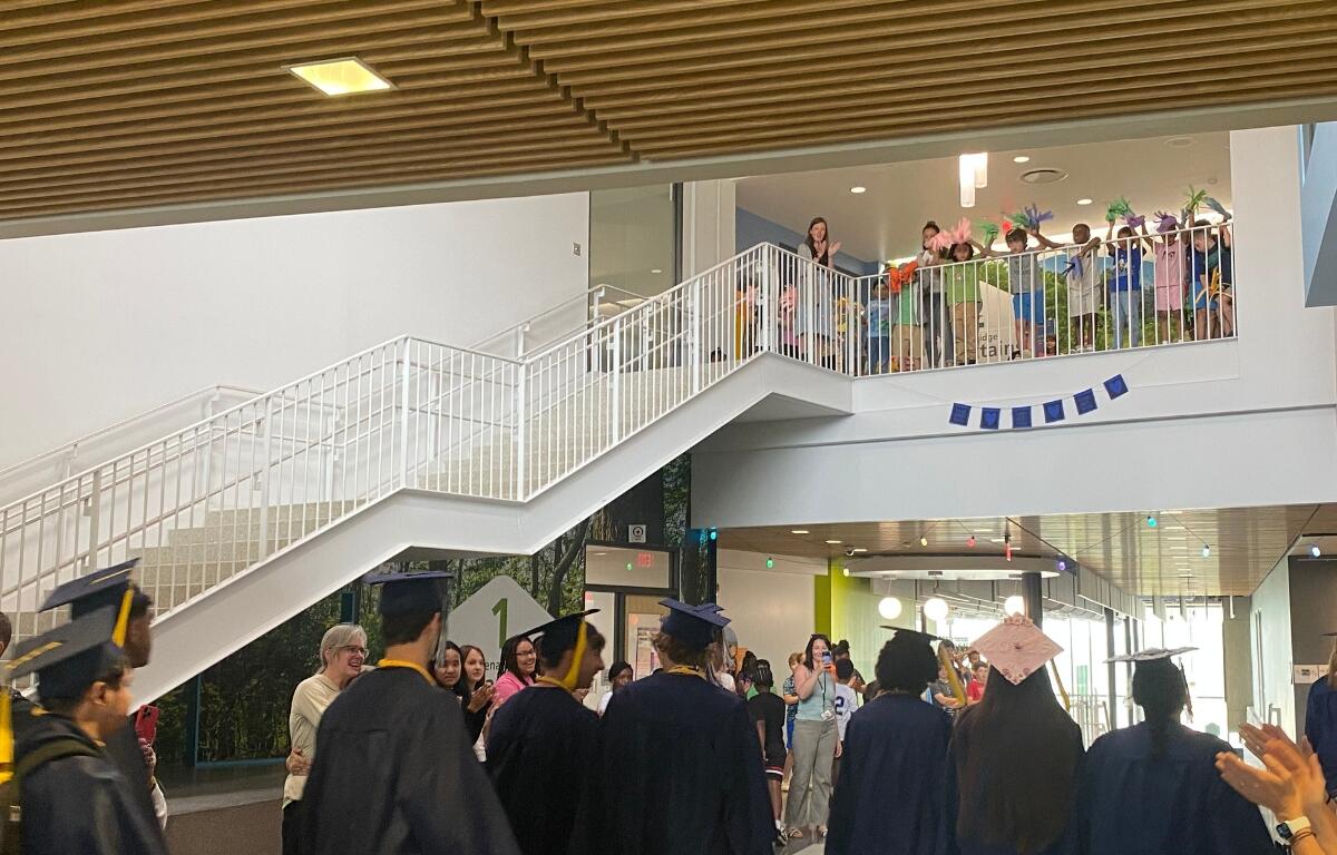 Seniors in caps and gowns walk through the hallways of their elementary school.