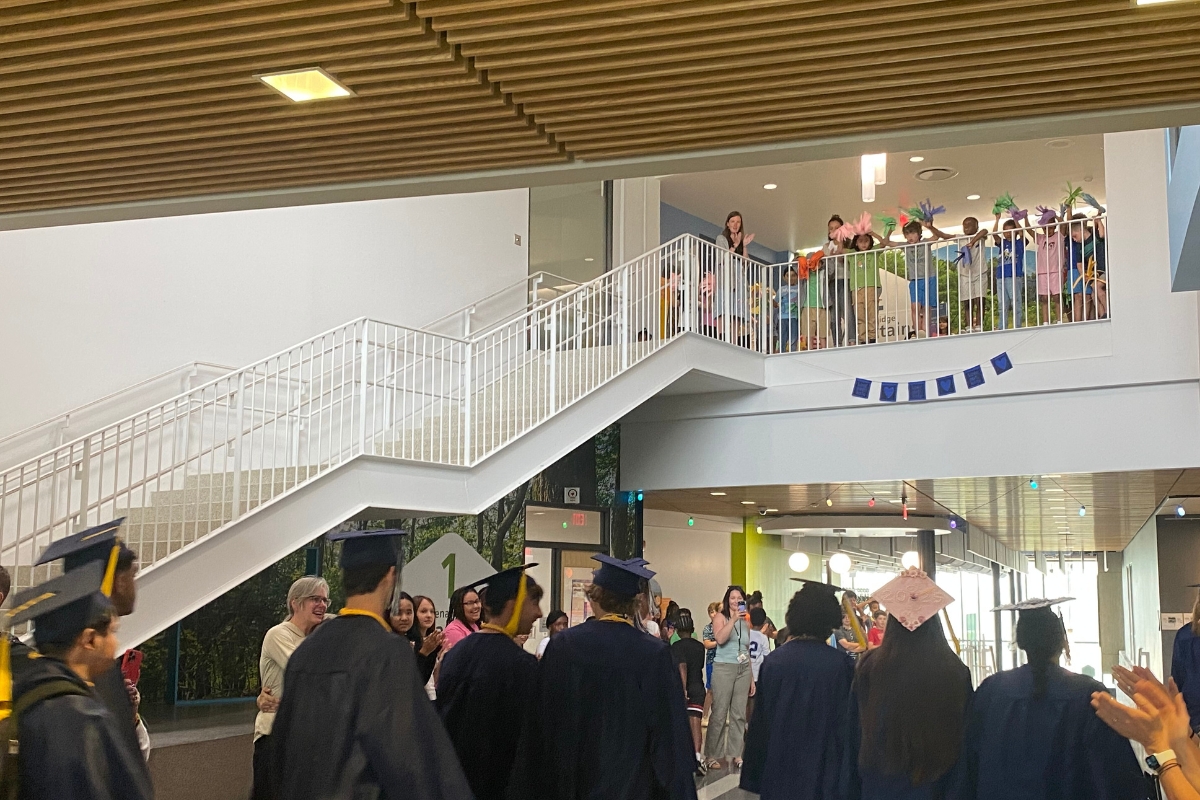 Seniors in caps and gowns walk through the hallways of their elementary school.
