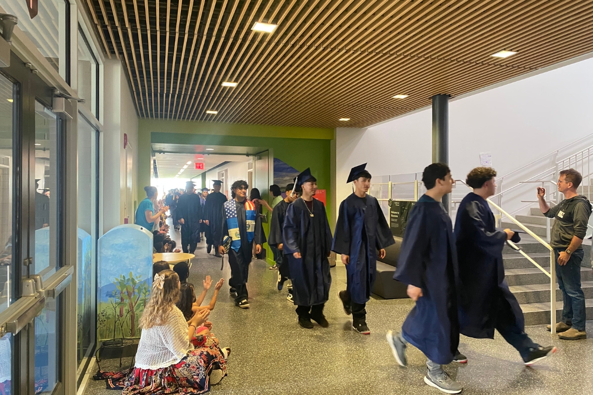 Seniors walks the hallways in their caps and gowns as elementary students cheer for them.