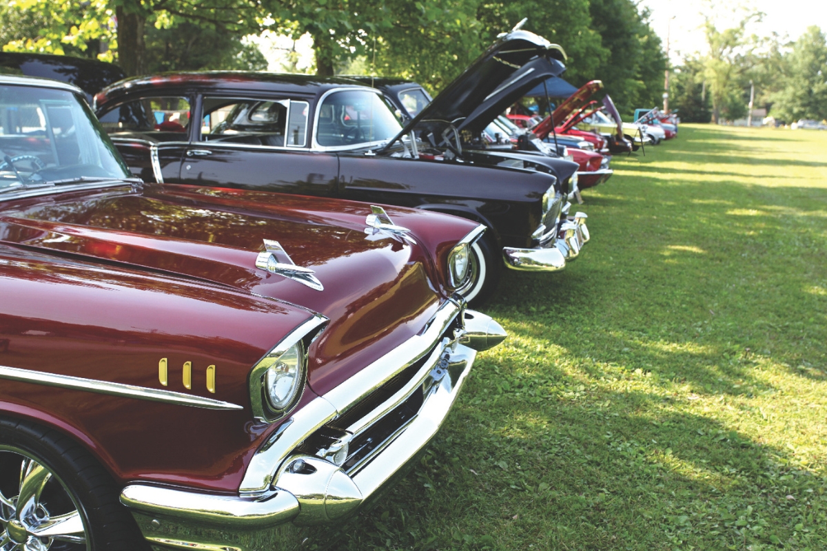 An old red car and black car sit in a row of other cars.