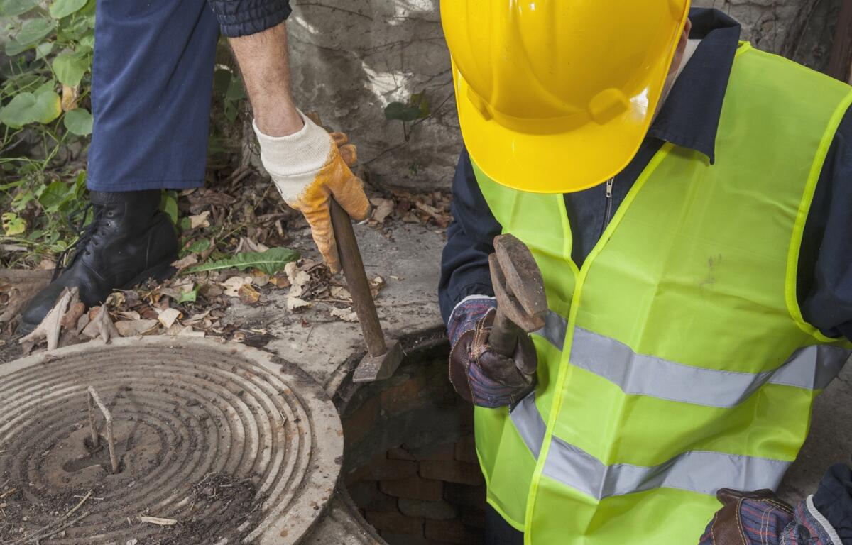 Two workers going into a manhole.