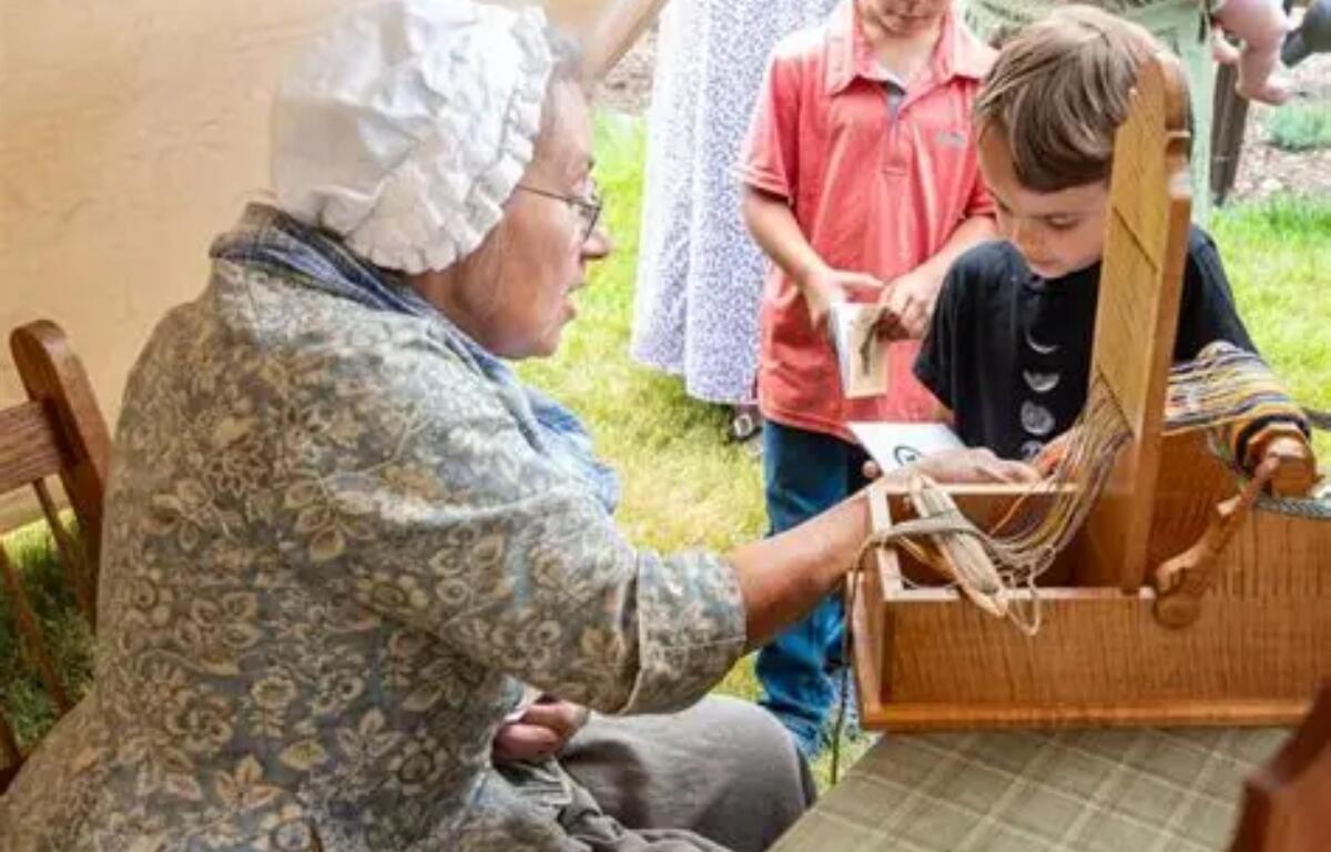 A lady demonstrating a clothing weaver to a few children.