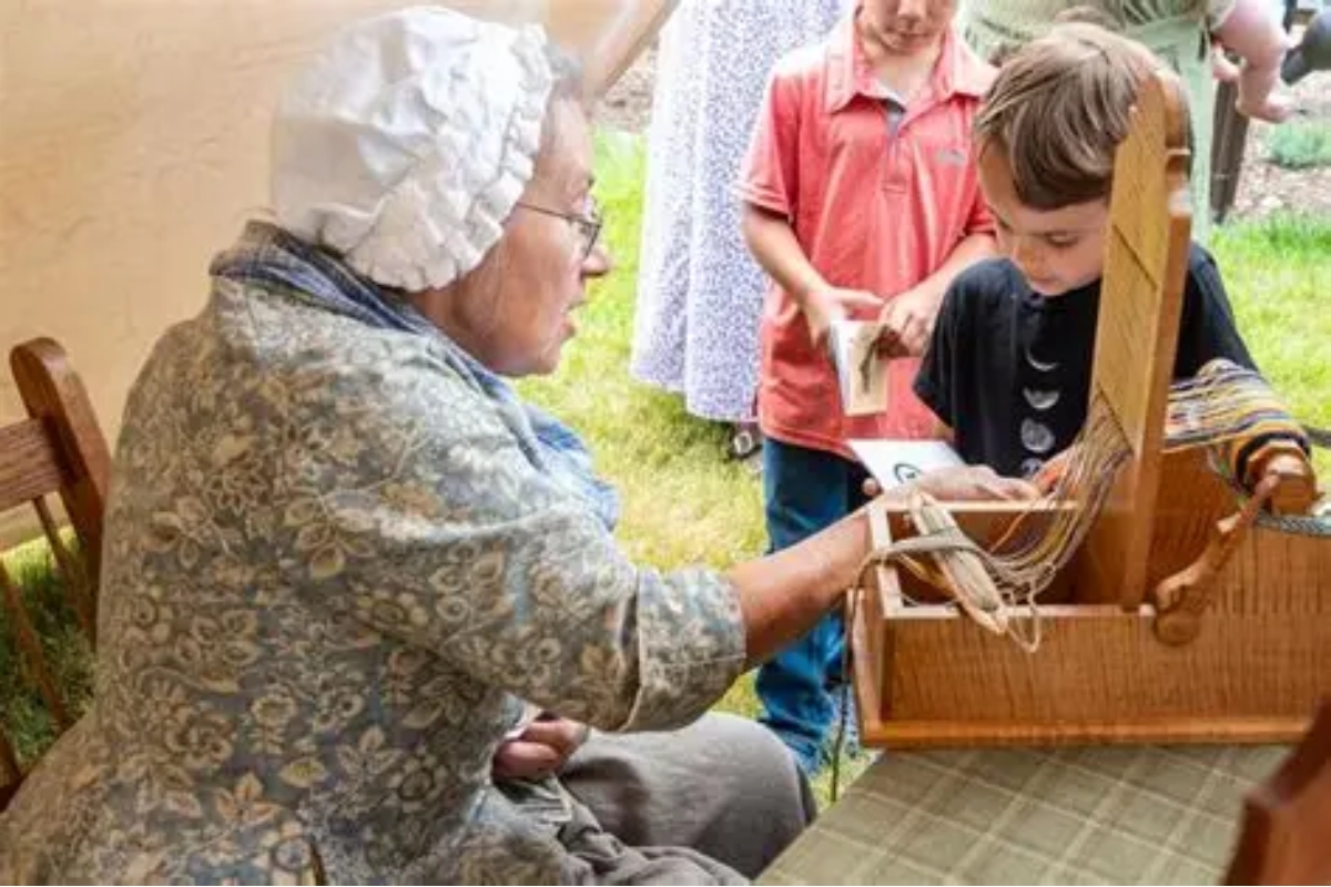 A lady demonstrating a clothing weaver to a few children.