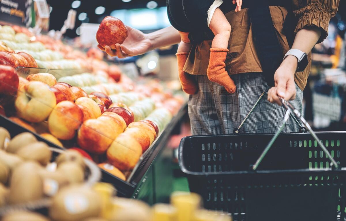 A customer picks up an apple to put in a grocery basket.