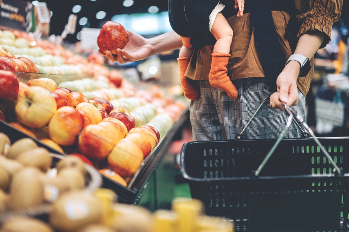 A customer picks up an apple to put in a grocery basket.