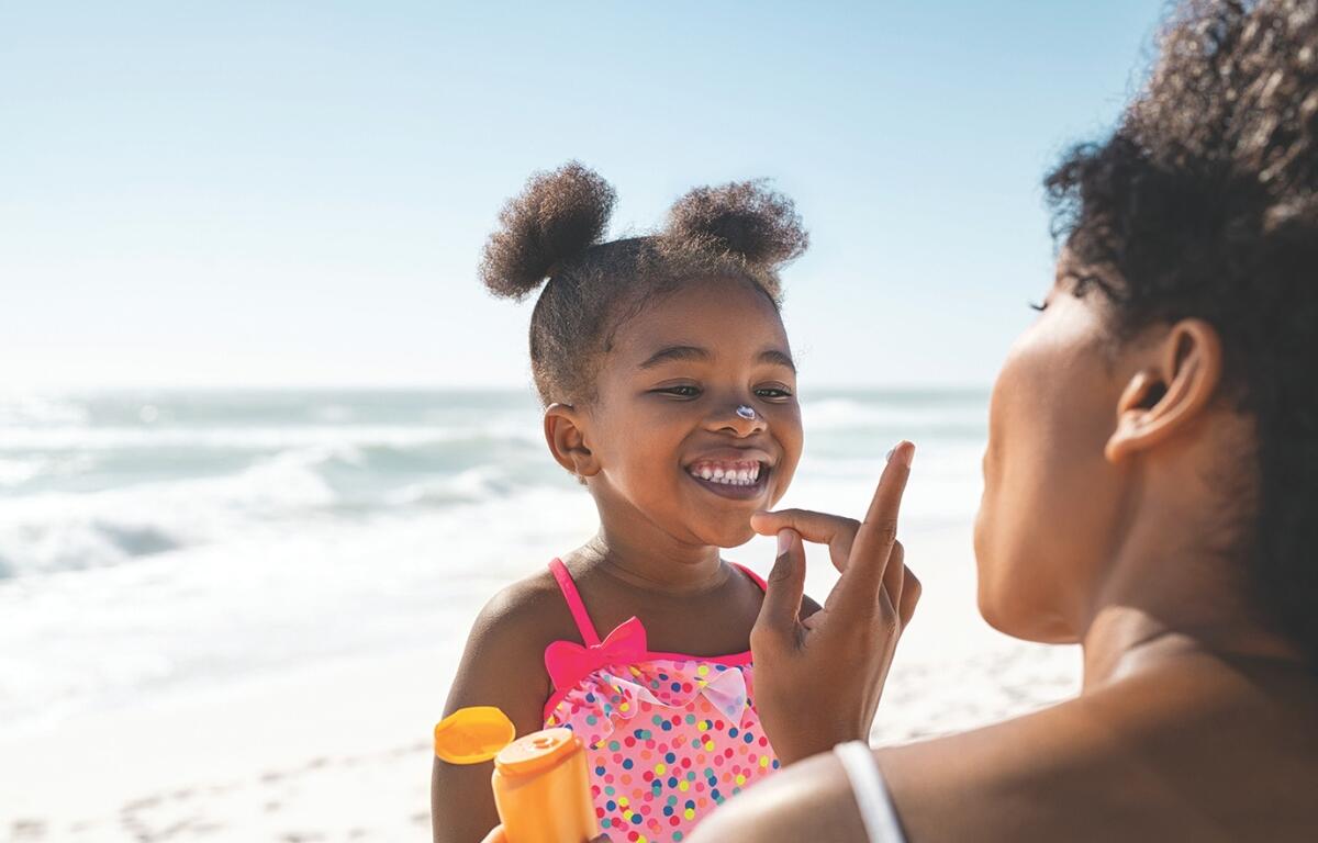 A little girl gets sunblock applied to her nose on the beach.
