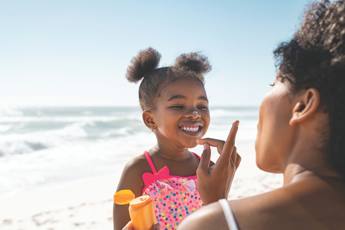 A little girl gets sunblock applied to her nose on the beach.