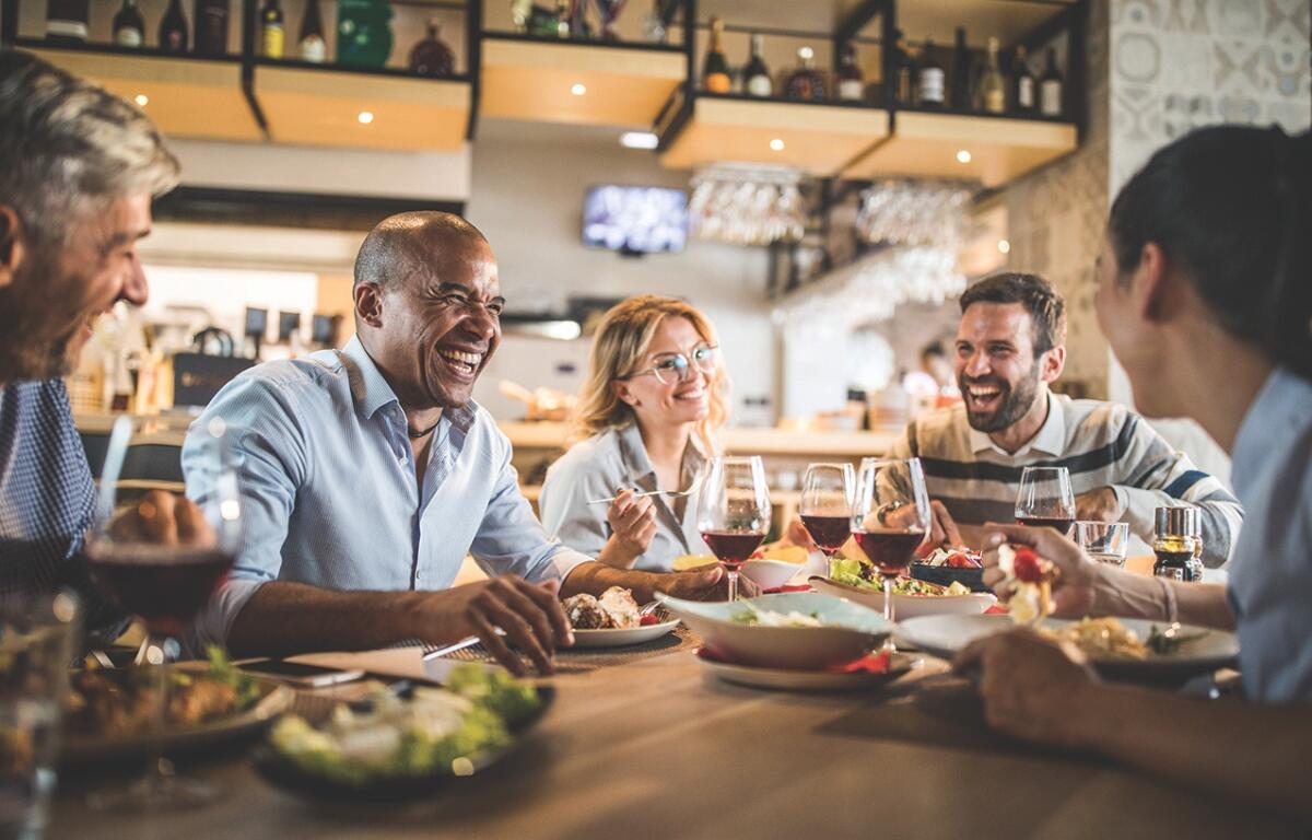 A group of people eating and laughing around a table in a restaurant.
