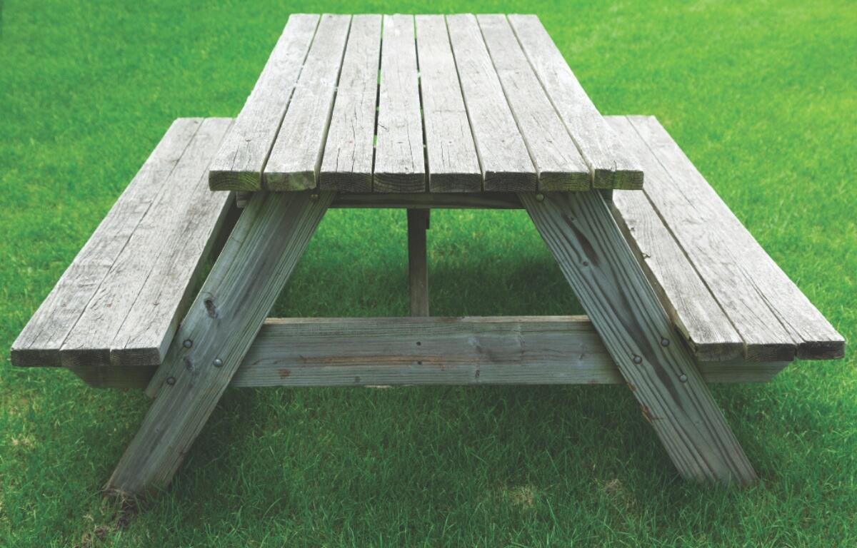 A wooden picnic table sitting in a grassy area.