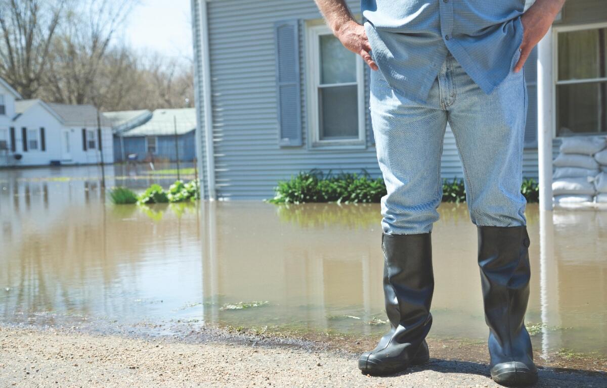 A person in rain boots standing in front of a flooded lawn.