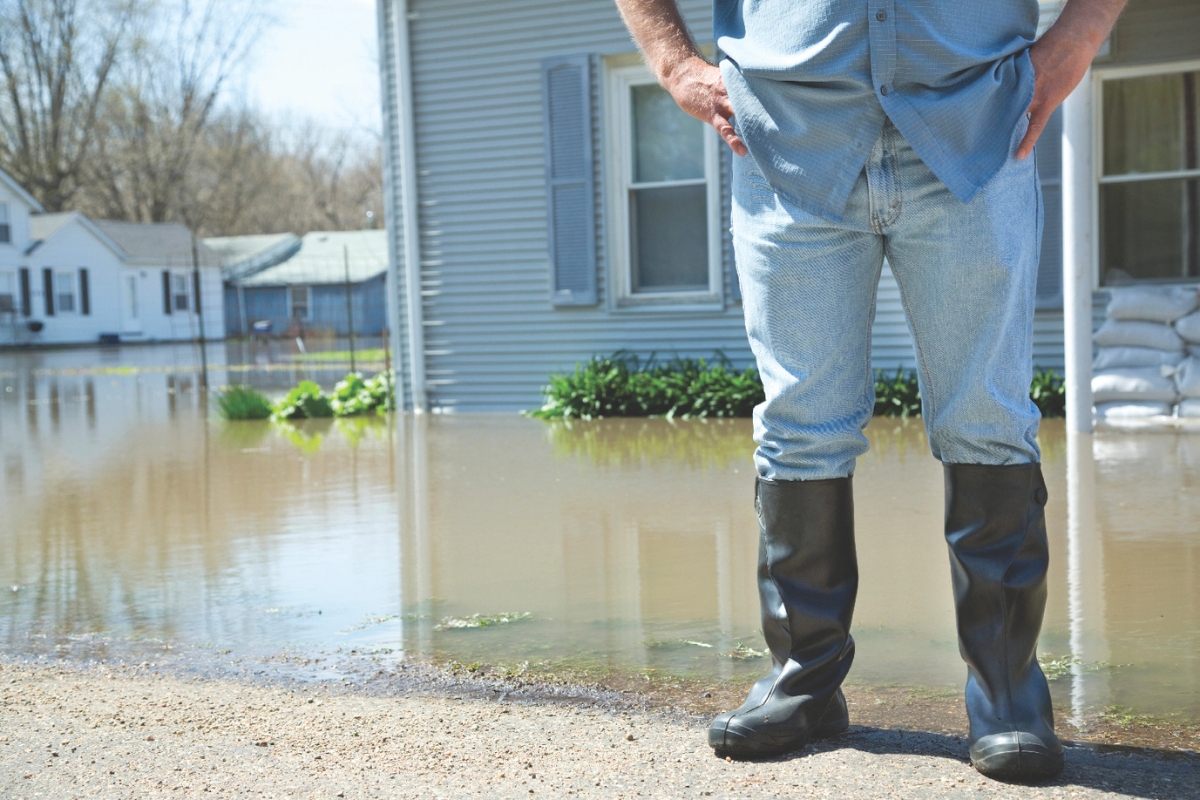 A person in rain boots standing in front of a flooded lawn.