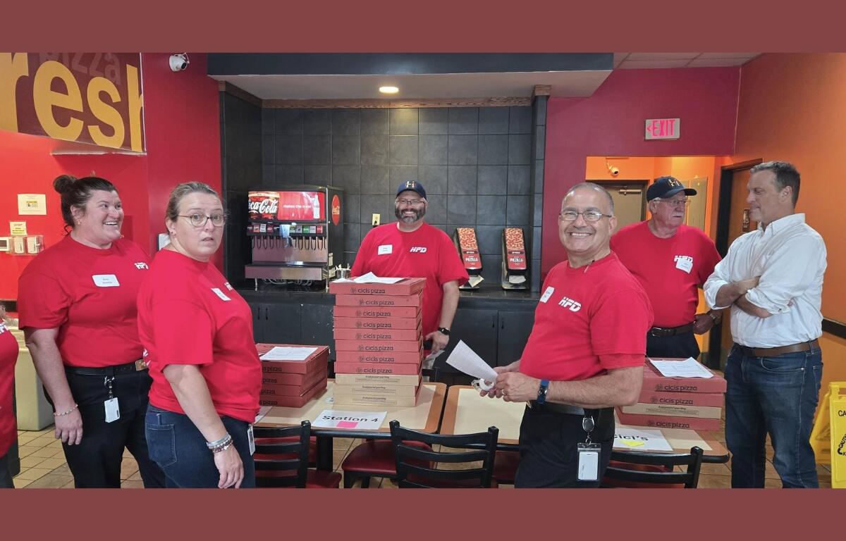 Many Harrisonburg Fire officials gather around stacks of pizzas to distribute.