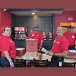 Many Harrisonburg Fire officials gather around stacks of pizzas to distribute.