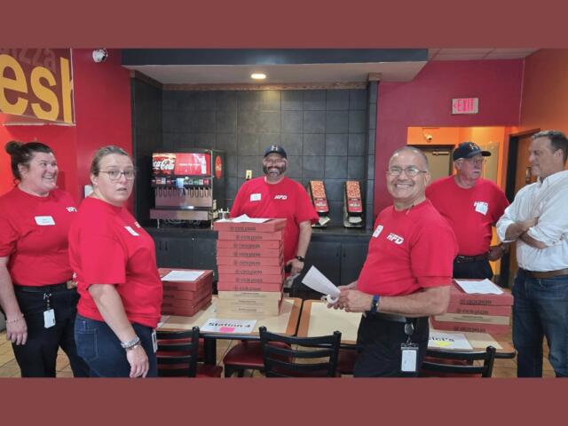 Many Harrisonburg Fire officials gather around stacks of pizzas to distribute.