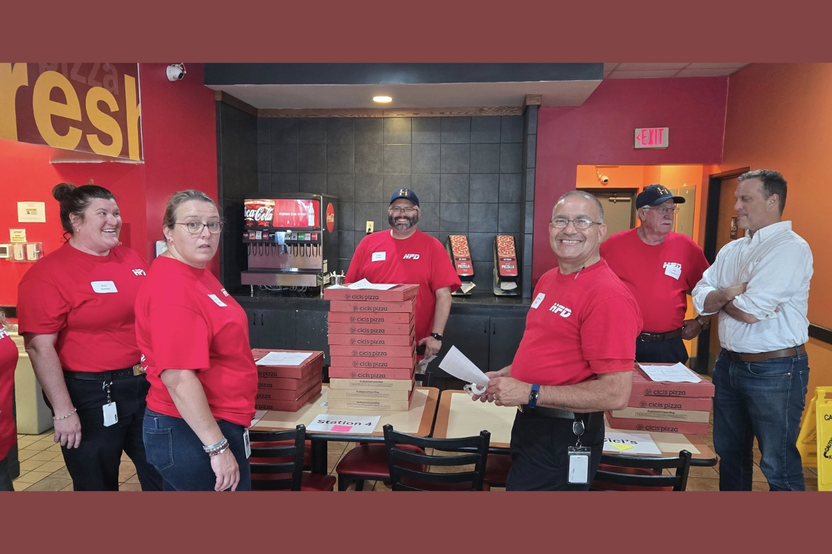 Many Harrisonburg Fire officials gather around stacks of pizzas to distribute.