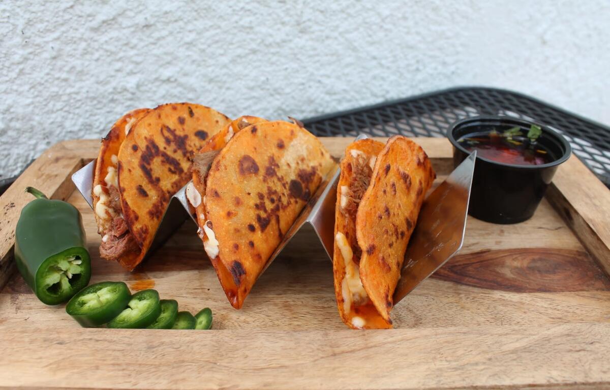 Three birria tacos on a cutting board with sliced jalapeno and salsa.