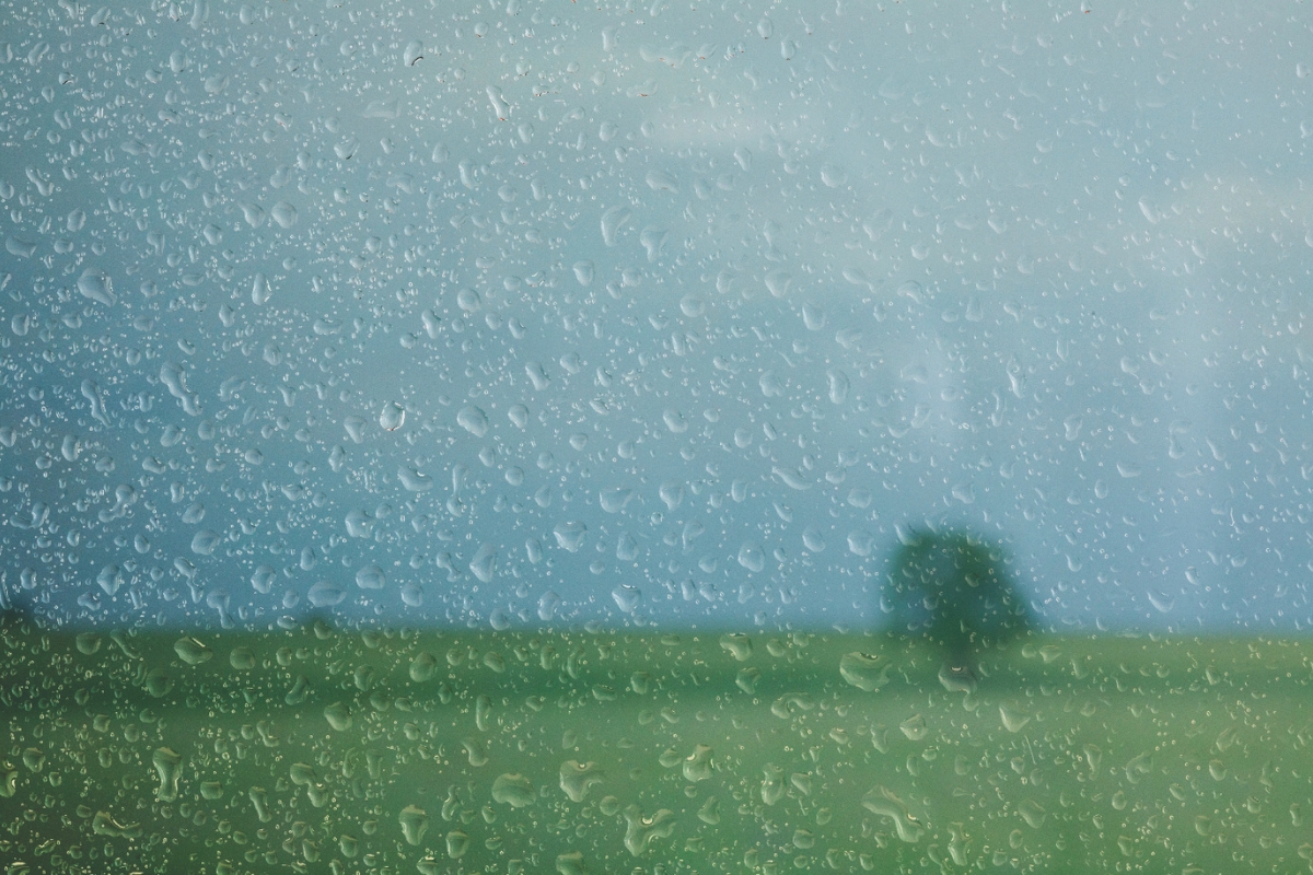Rain drops on a window overlooking a grassy field.