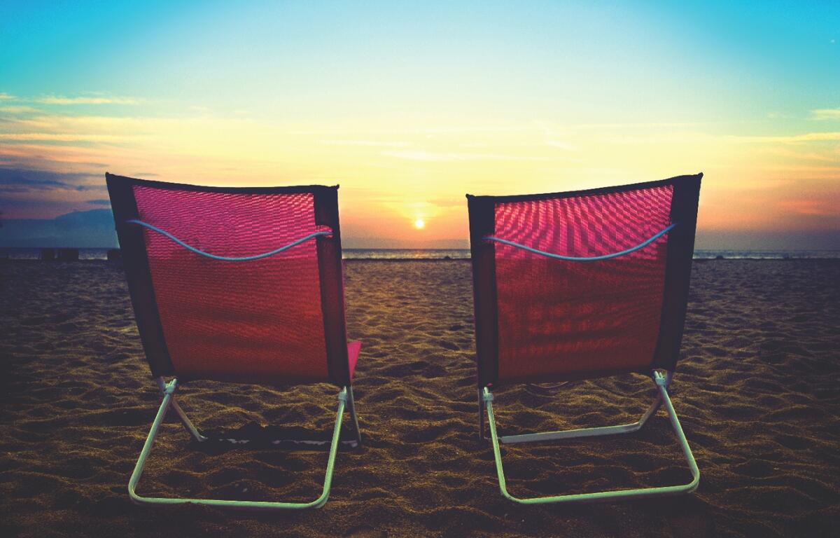 Two beach chairs sitting in the sand on the beach at sunset.