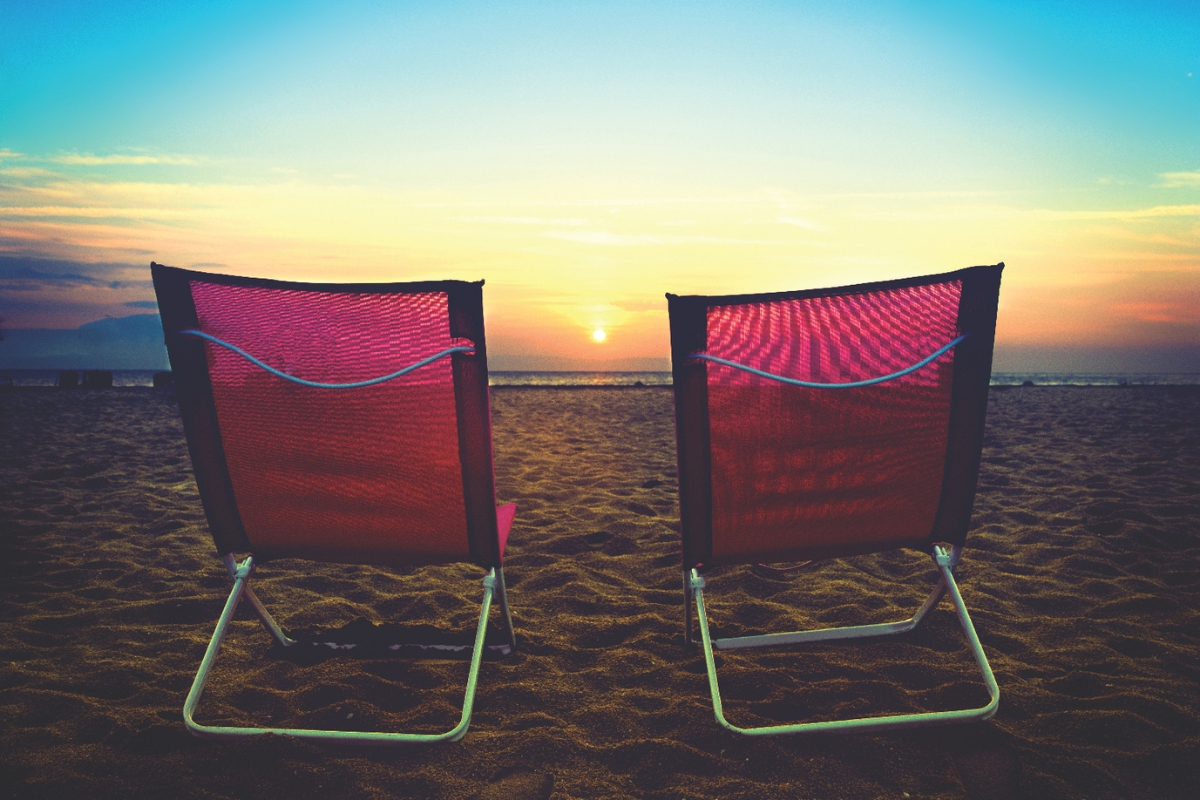 Two beach chairs sitting in the sand on the beach at sunset.